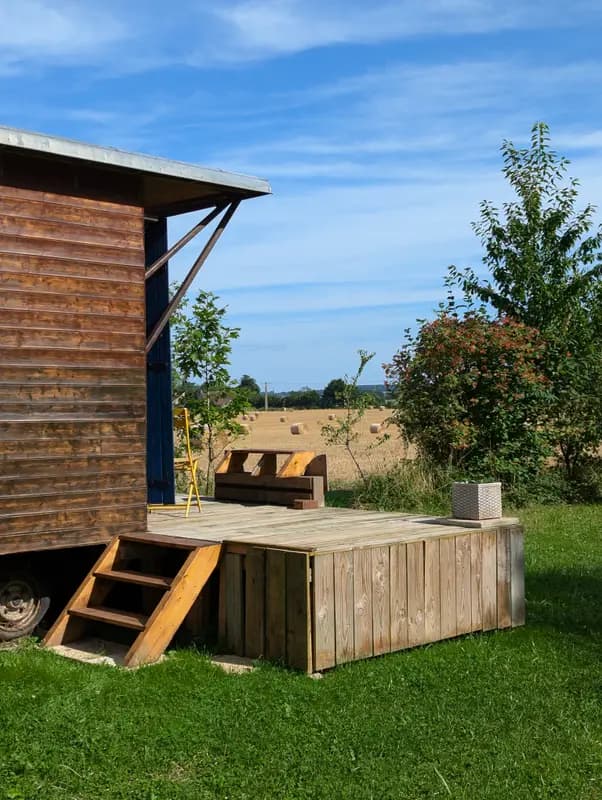 Rustic wooden cabin terrace overlooking golden hay bale fields, outdoor seating area with countryside dining ambiance