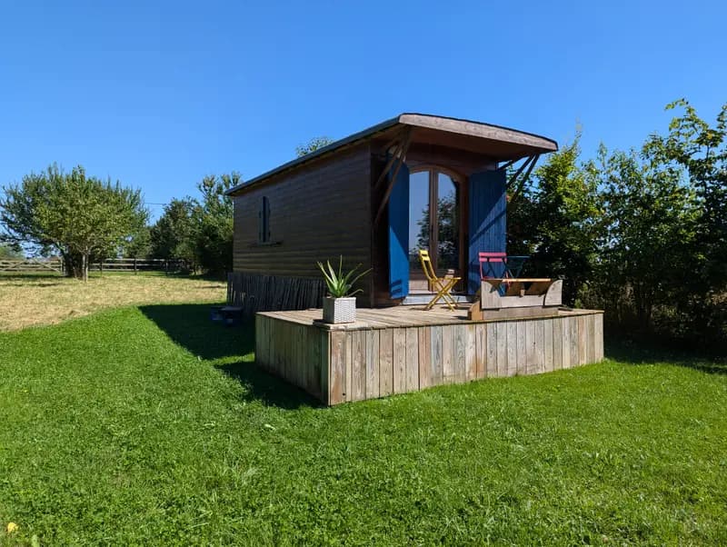 Rustic wooden cabin with blue doors, outdoor deck seating, and lush green surroundings on a sunny day.