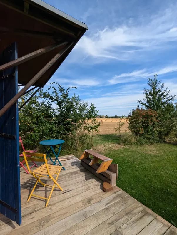 Rustic outdoor terrace with colorful bistro chairs overlooking golden hay fields under a sunny blue sky